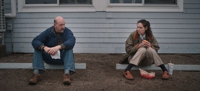 A man and woman sit on a kerb and talk over lunch.
