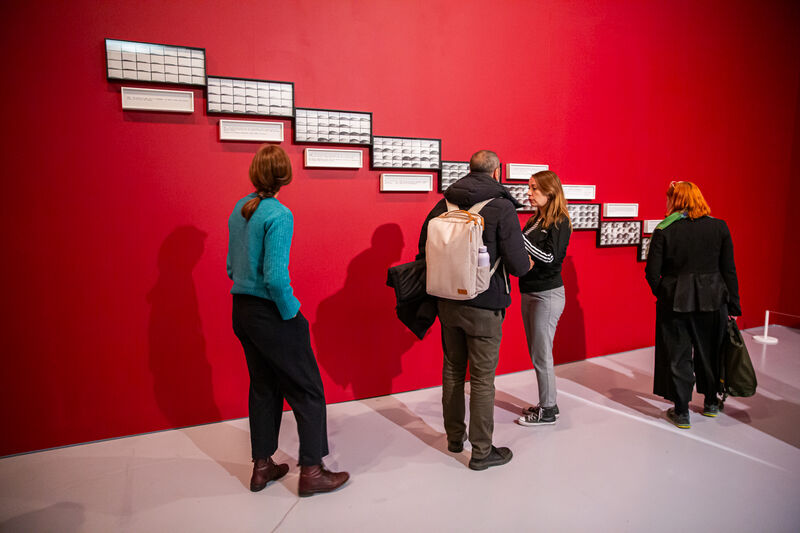 a red gallery wall with black and white images on it and visitors looking at it 