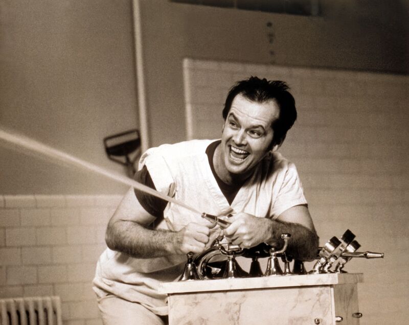 A man wearing white hospital pyjamas shoots water from a fountain while laughing