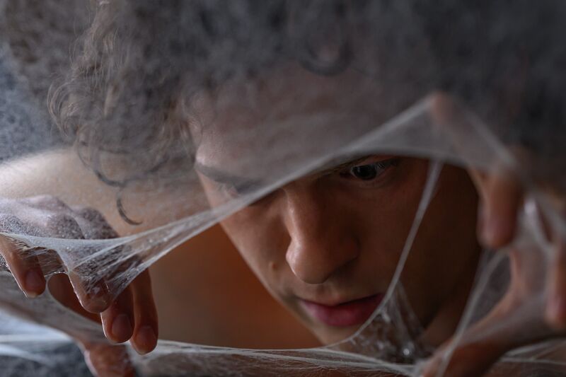 A man pulls apart a spider web with his hands whilst looking through the gap