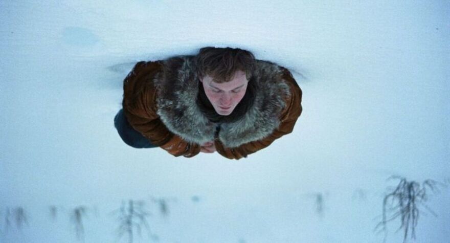 An upside-down photo. A young man lies on his back in a snowy wilderness.