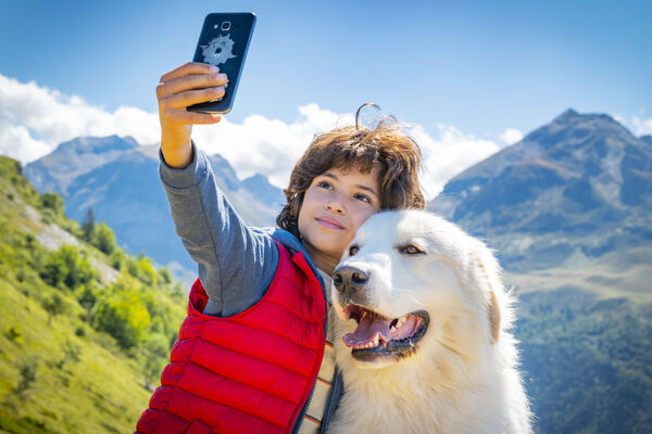 A boy takes a selfie with his dog in the Alpine mountains