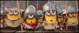Group of small yellow Minion-style characters dressed as medieval soldiers, wearing metal helmets and ragged tunics, holding spears in formation inside a stone castle setting.