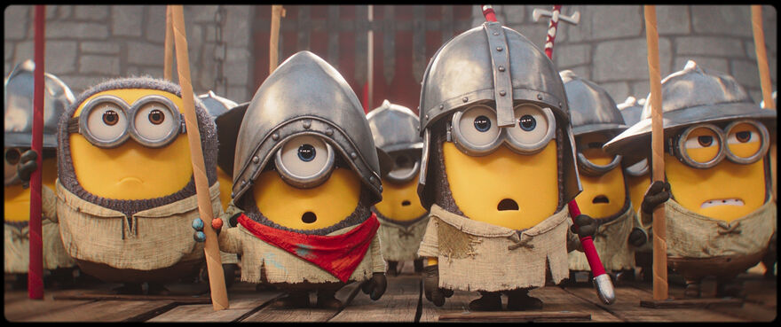Group of small yellow Minion-style characters dressed as medieval soldiers, wearing metal helmets and ragged tunics, holding spears in formation inside a stone castle setting.