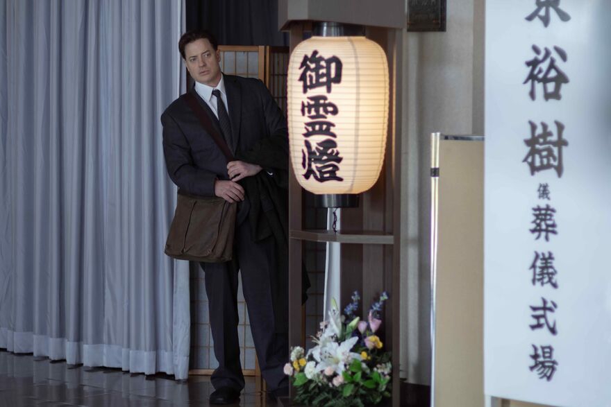 A man wearing a suit stands next to a Japanese paper lantern with flowers beneath it.