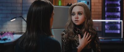 A humanoid robot with long blonde hair and blue eyes talks to someone in a lab.