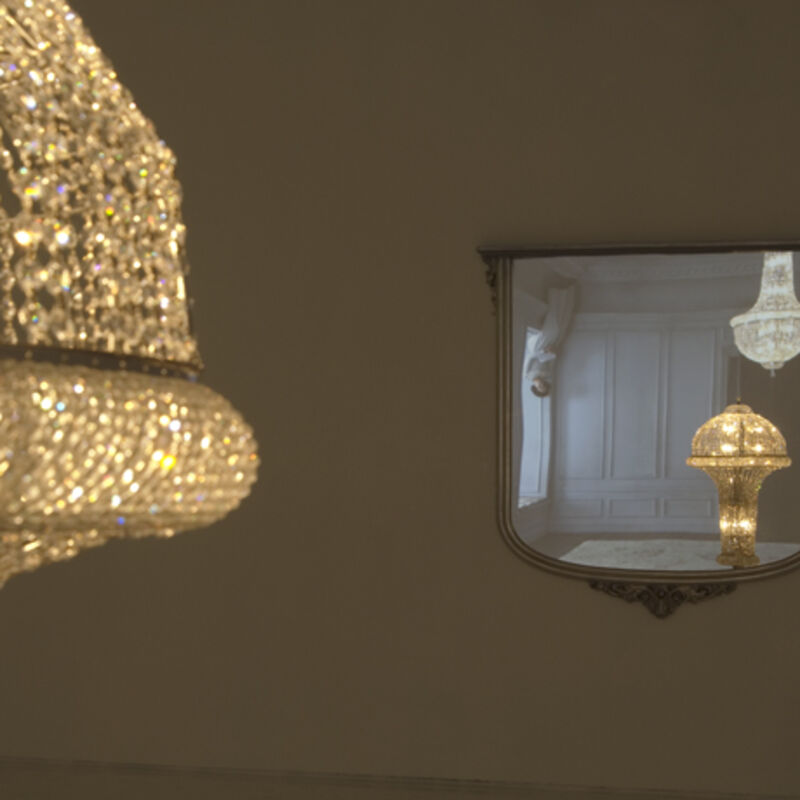 From Matthew Buckingham’s exhibition. A golden, sparkling chandelier is reflected upside-down in a mirror.