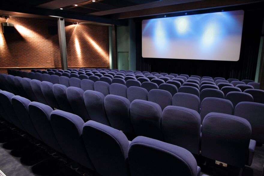 Cinema 1. The chairs are blue and there is a cinema screen at the front.