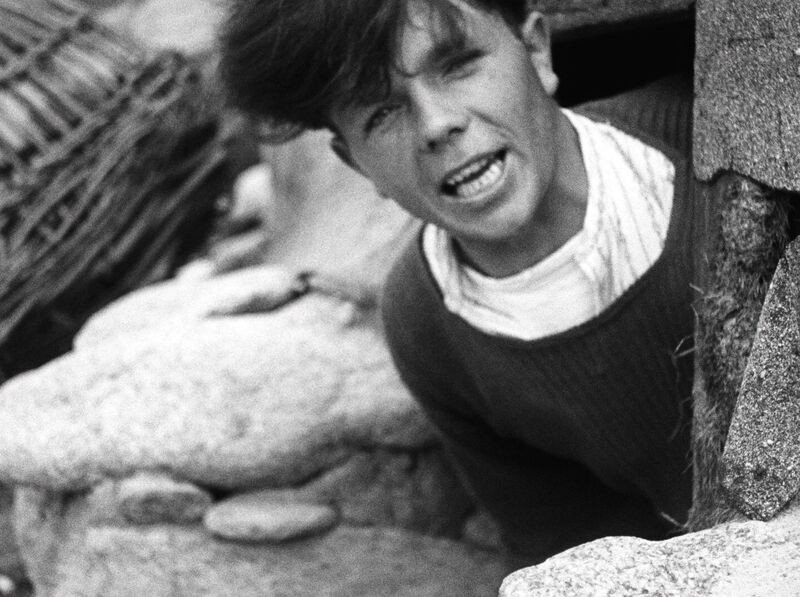 A man looks at the camera, he is on a rocky beach
