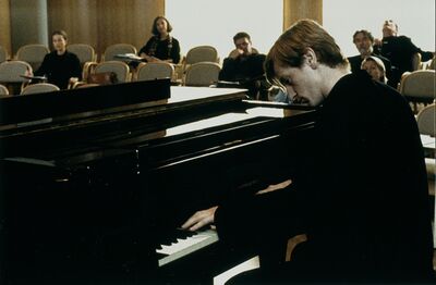 A man plays the piano in front of a small audience.
