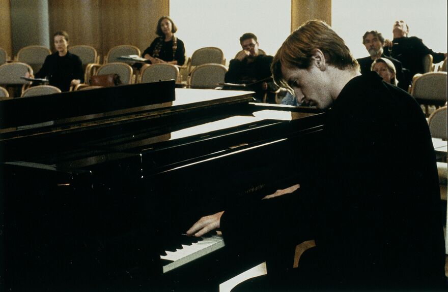 A man plays the piano in front of a small audience.