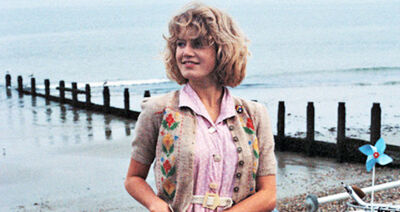 A girl stands in front of the sea with a 80s style