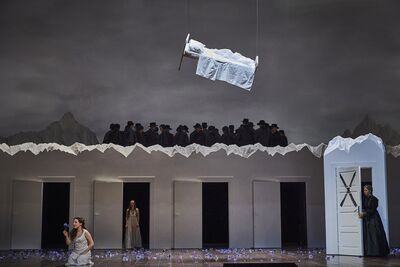 A bed flies over the stage as a woman sings and a chorus of shadowy figures surround her.