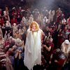 A woman with long hair and a long white dress floating above a crowd