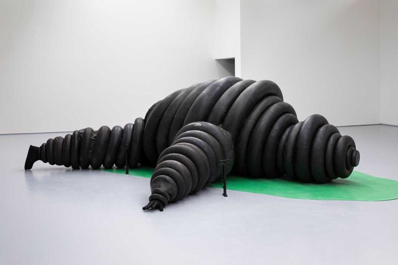 A michelin man madę of black tyre sculptures lying on a green cut out of a banana leaf 