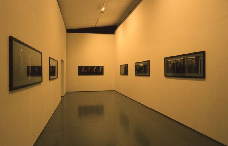 A white gallery wall is covered in rectangular frames with black photographs in them.