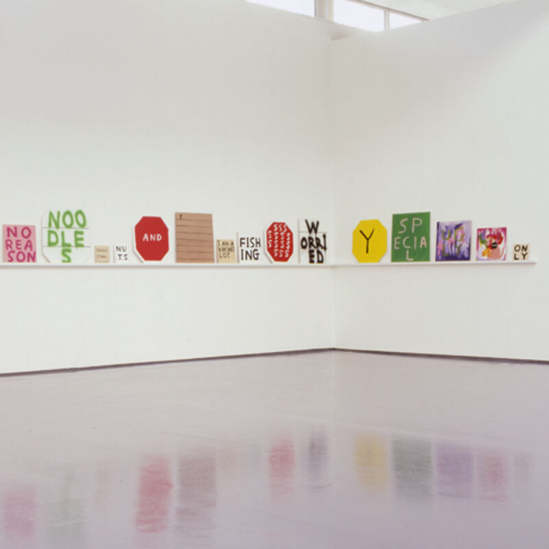 From David Shrigley's exhibition in DCA Gallery. A shelf wraps round the gallery wall, with numbers colourful spray-painted canvas. These have words or letters on them.