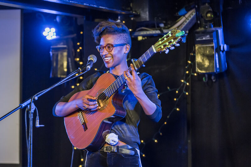 A woman smiles while playing guitar on stage