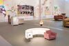A gallery space with bright paintings on the wall, with paint directly on the walls - in the centre of the gallery are a Lightbox and a small armchair 
