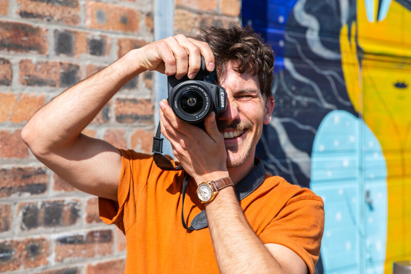 Person smiling a they take a picture with a digital camer