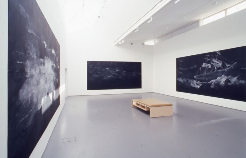 Three large black canvases hang on DCA's white galleries walls. The black canvases have white marks on them with chalk.