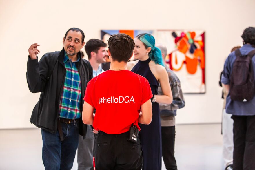 A person standing in a gallery wearing a red t-shirt with helloDCA on the back.