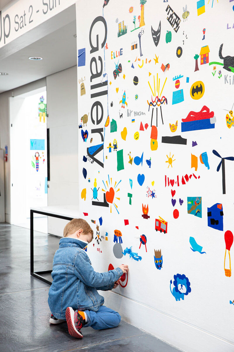 Child sticking vinyl to the wall outside of Gallery 1 to create a giant mural