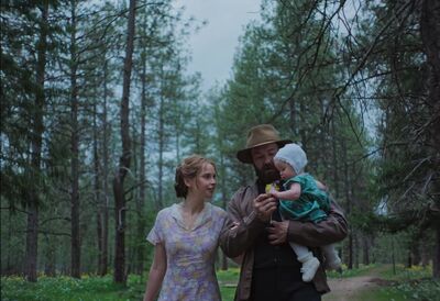 A man, woman and baby, wearing vintage clothes, walk through a forest today.