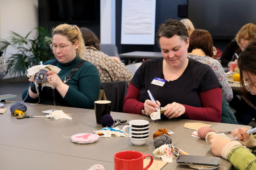 Two people sitting at a table doing needle punching at a Craft Sunday workshop