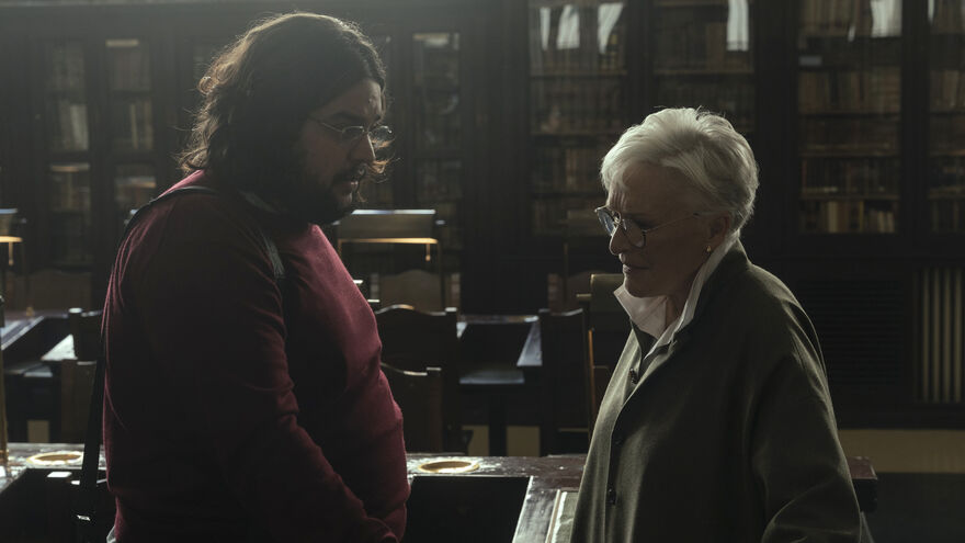 A bearded man and an older woman converse in a library