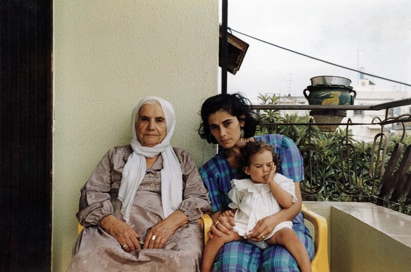 A family portrait taken on a balcony shows an elderly woman and a younger woman. The younger woman has a baby on her lap.