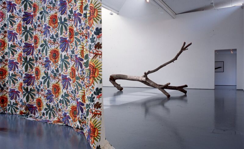 A colourful curtain covered in flowers hangs in DCA Galleries, behind this is a large tree branch.