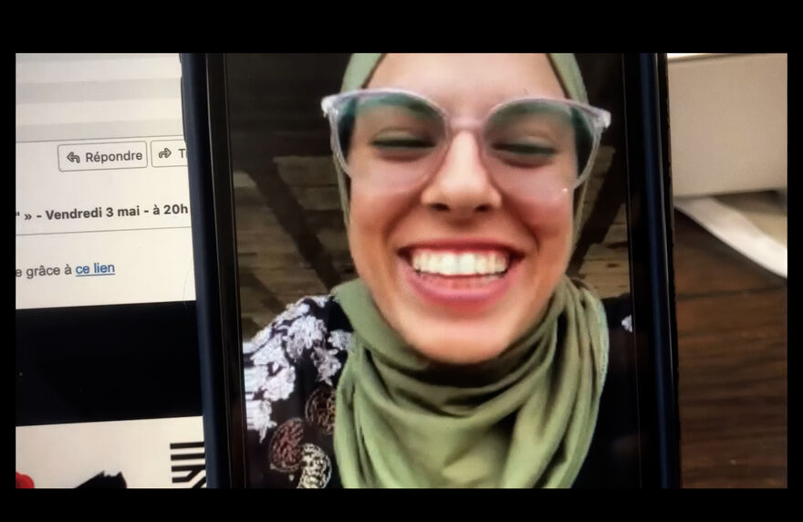 The image on a phone of a smiling women in a headscarf wearing glasses