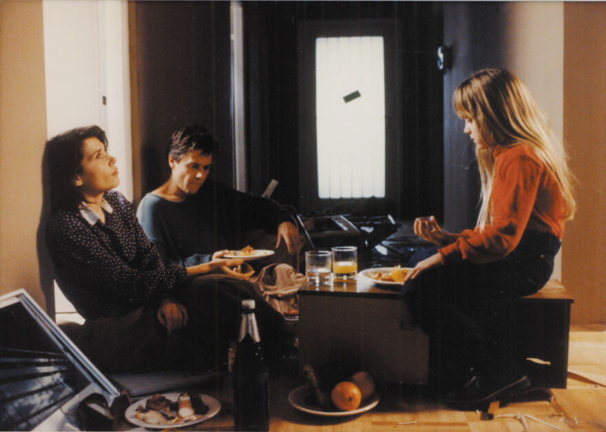 Parents and a young girl sit on the floor of an empty apartment eating breakfast quietly.