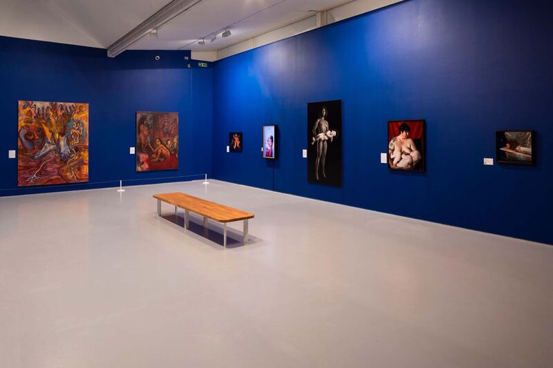 A gallery space with the walls painted deep blue with large paintings photography and video works on display