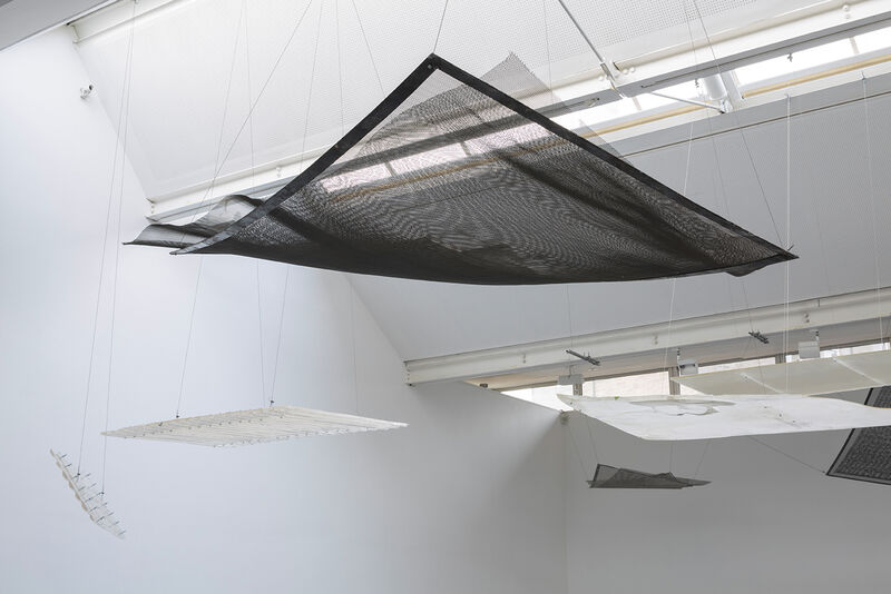 Photograph shows a series  of hanging works as part of an installation. Black and white sheets of metal are suspended from the ceiling.