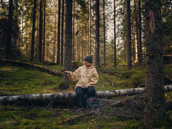 Teen girl with blonde hair and a beanie hat sits on a log in the forest