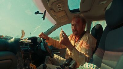 A panicked man holds a bullet while driving a car.