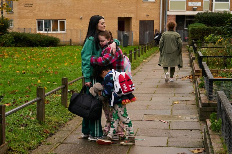A woman stands on a path hugging two little girls.