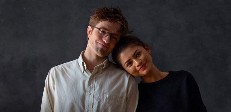A man and a woman at a photoshoot smile and the woman rests her head on the man's shoulder