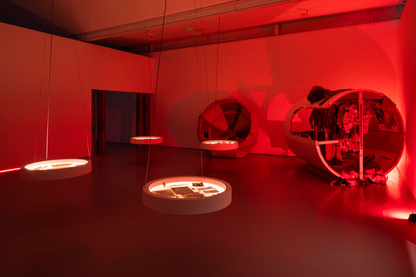 A gallery with red light, several backlit circular vitrines and displays of film costumes.