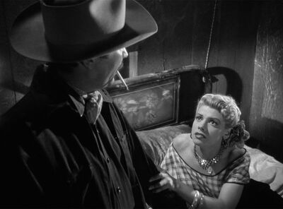 A black-and-white still shows a woman in a 1940s dress sitting on a bed, holding the arm of a man smoking a cigarette