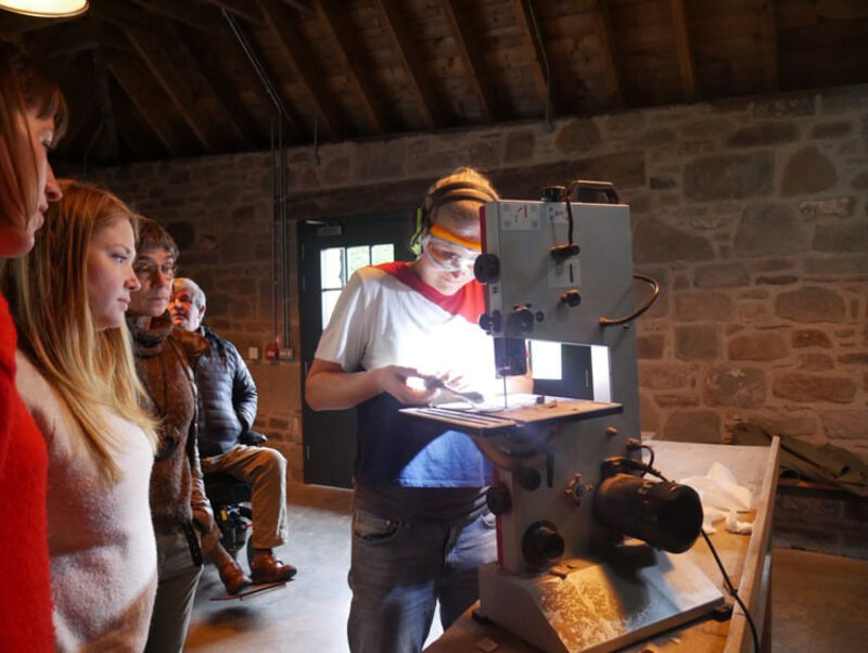 Louise Forbes using a machine to cut wood while a class of people watch