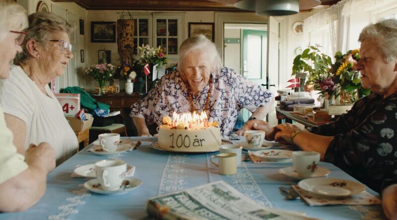 A smiling woman blows out candles on a cake for her one hundredth birthday.