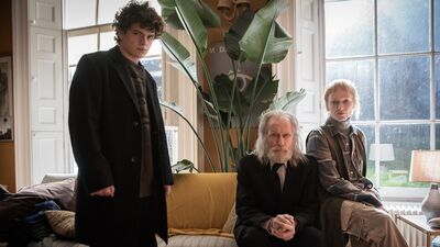 A young man and woman sit with their elderly father in a grand home.
