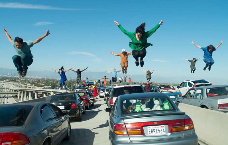 People leap into the air in unison above their cars on a packed freeway