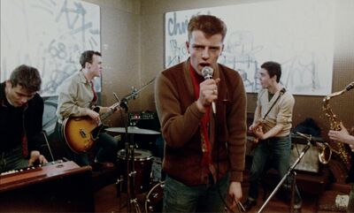 A young band plays while the singer looks at the camera