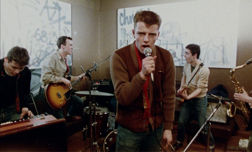 A young band plays while the singer looks at the camera