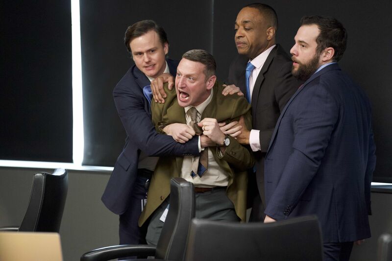  A man in a brown suit yells while three other men hold him back.