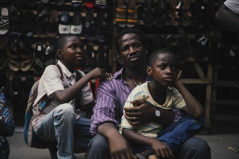 A man sits outside a shoe shop with two young boys